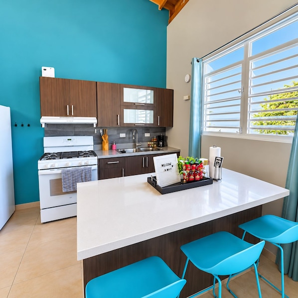 A modern kitchen with a central island, bar stools, and a view of greenery outside.