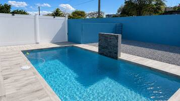 Una piscina rectangular con superficie de agua azul cristalina, rodeada por un deck de baldosas de color claro.
