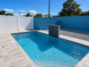 Una piscina rectangular con superficie de agua azul cristalina, rodeada por un deck de baldosas de color claro.