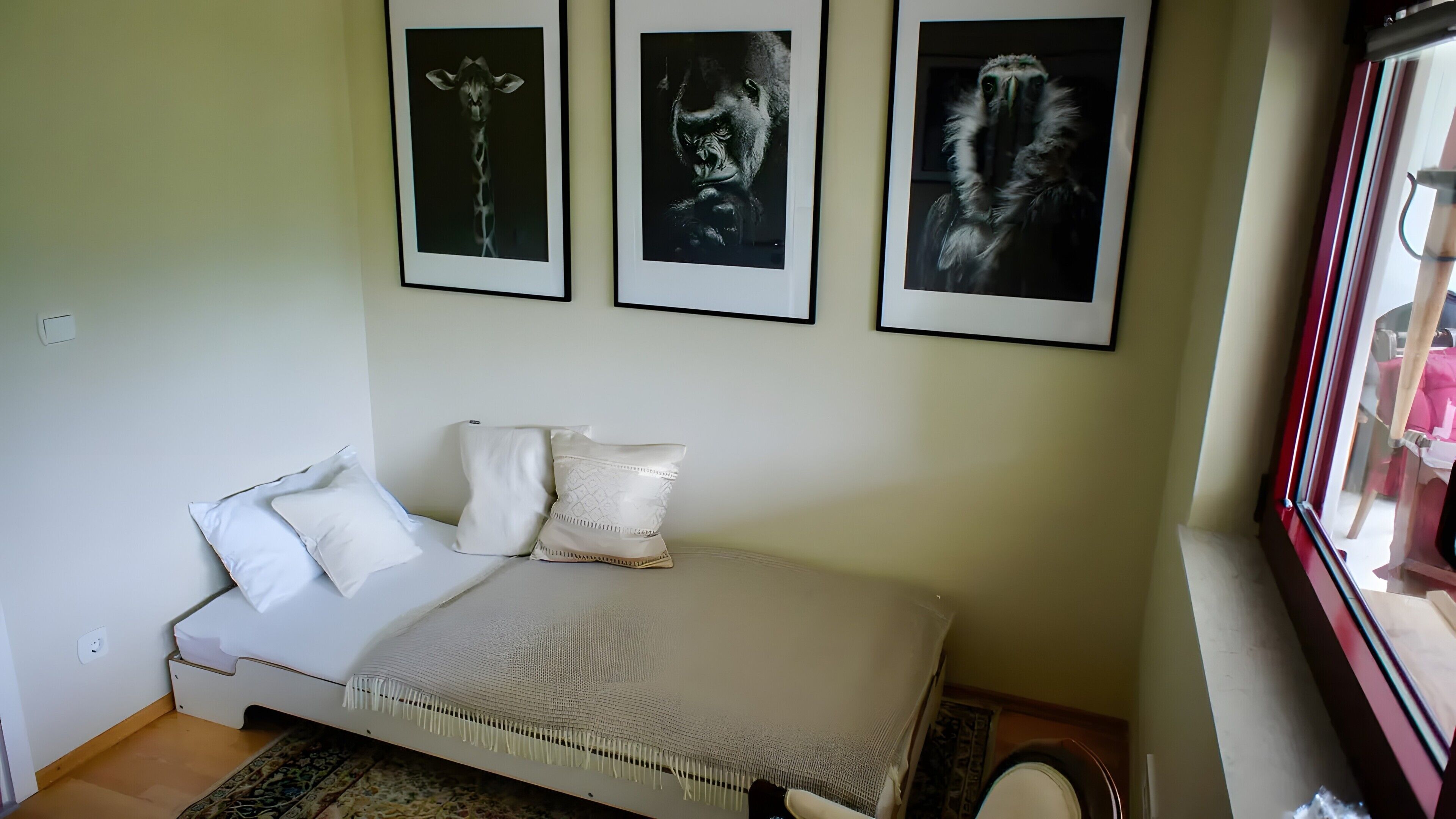 A bedroom with a bed, pillows, a window, and three framed pictures on the wall.