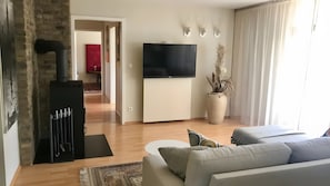 Een woonkamer met een televisie, een bank, een bijzettafeltje, een vloerkleed en een kamerplant.