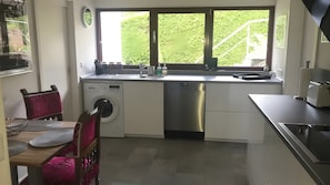 Een compacte keuken met een wasmachine, een spoelbak en een raam met uitzicht op groen.