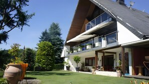 Una casa moderna de dos pisos con un balcón grande, césped cuidado y plantas en macetas.