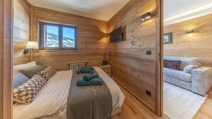 A wooden-paneled room with a bed, a nightstand, a TV, and a sofa. - Walking distance—historic center—sleeps 6 (Megève)
