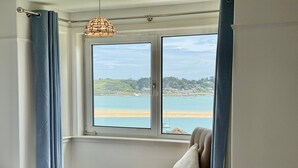 A bedroom with a large window, a chair, a bed, and a hanging light fixture. - 22 Treverbyn Road  - Spacious Home with amazing estuary views (Padstow)