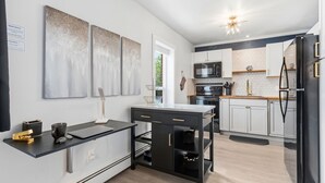 Una cocina moderna con encimera negra, armarios blancos, refrigerador negro y microondas.