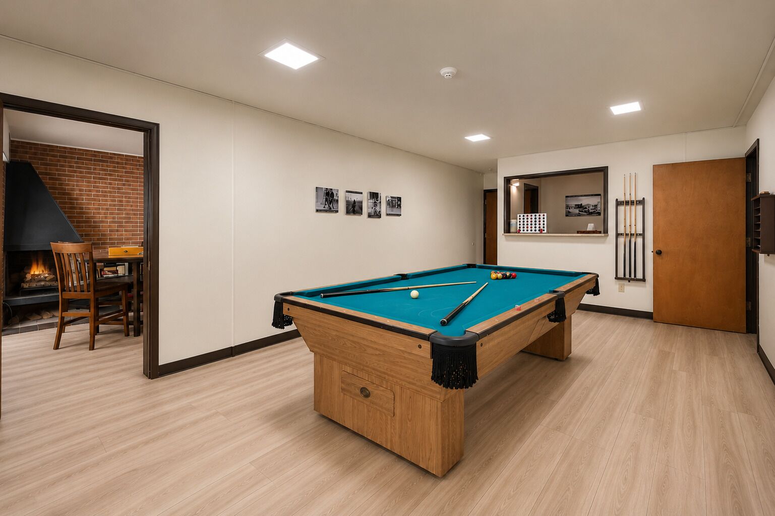 A pool table in a room with a fireplace, a dining area, and a door leading to another room.