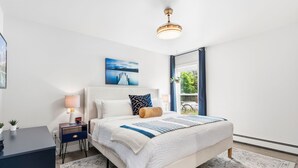Un dormitorio con cama, mesita de noche, lámpara y un cuadro en la pared.