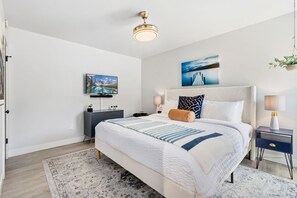 A bedroom with a bed, bedside tables, a television, and artwork on the walls. - Coastal Comfort Steps From Csu, Pool, Gym, Sauna (Fort Collins)