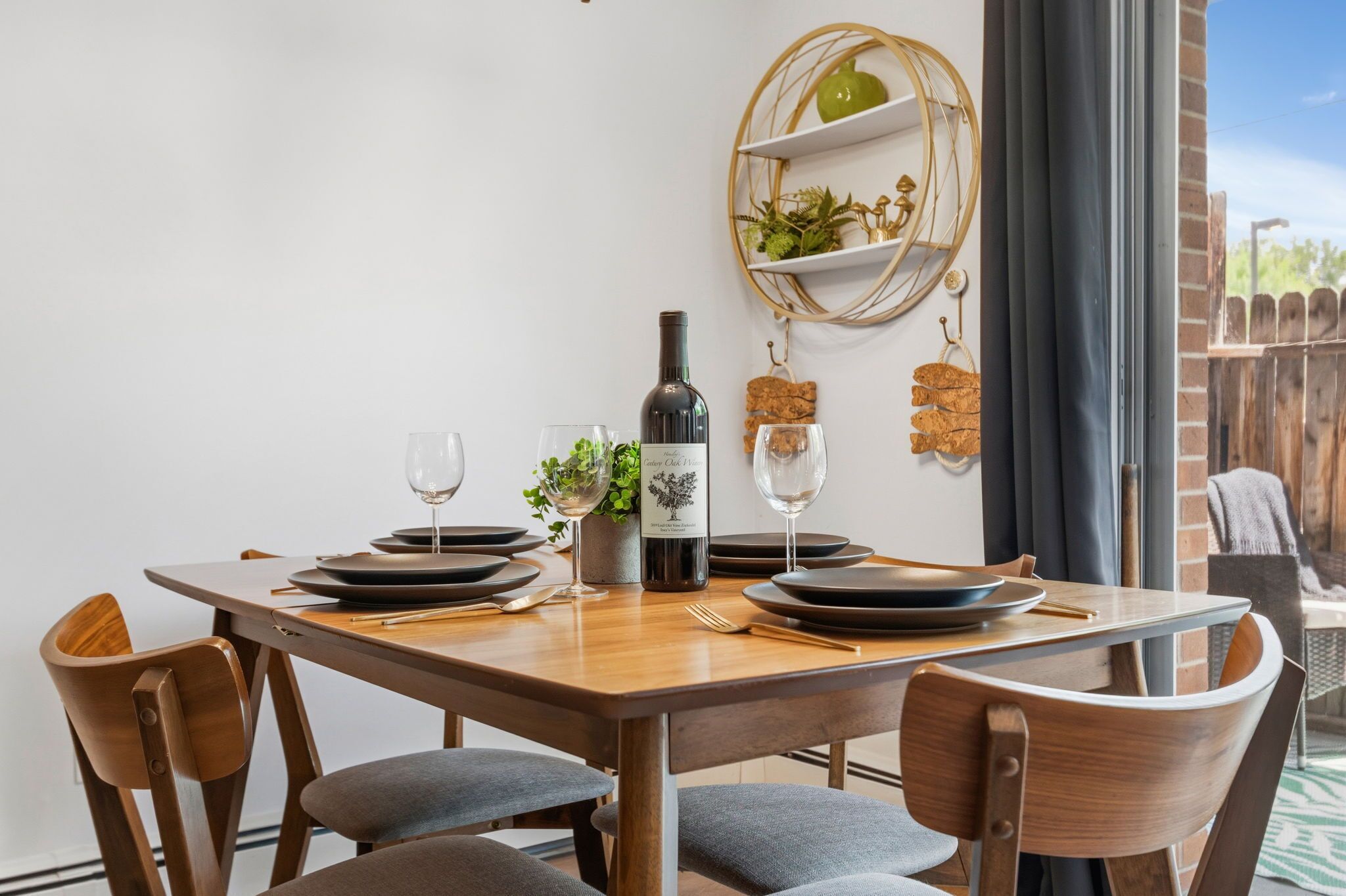A dining table set with plates, glasses, and a bottle of wine, surrounded by chairs.
