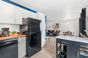 A modern kitchen with a black refrigerator, white cabinets, and a wooden countertop. - Coastal Comfort Steps From Csu, Pool, Gym, Sauna (Fort Collins)