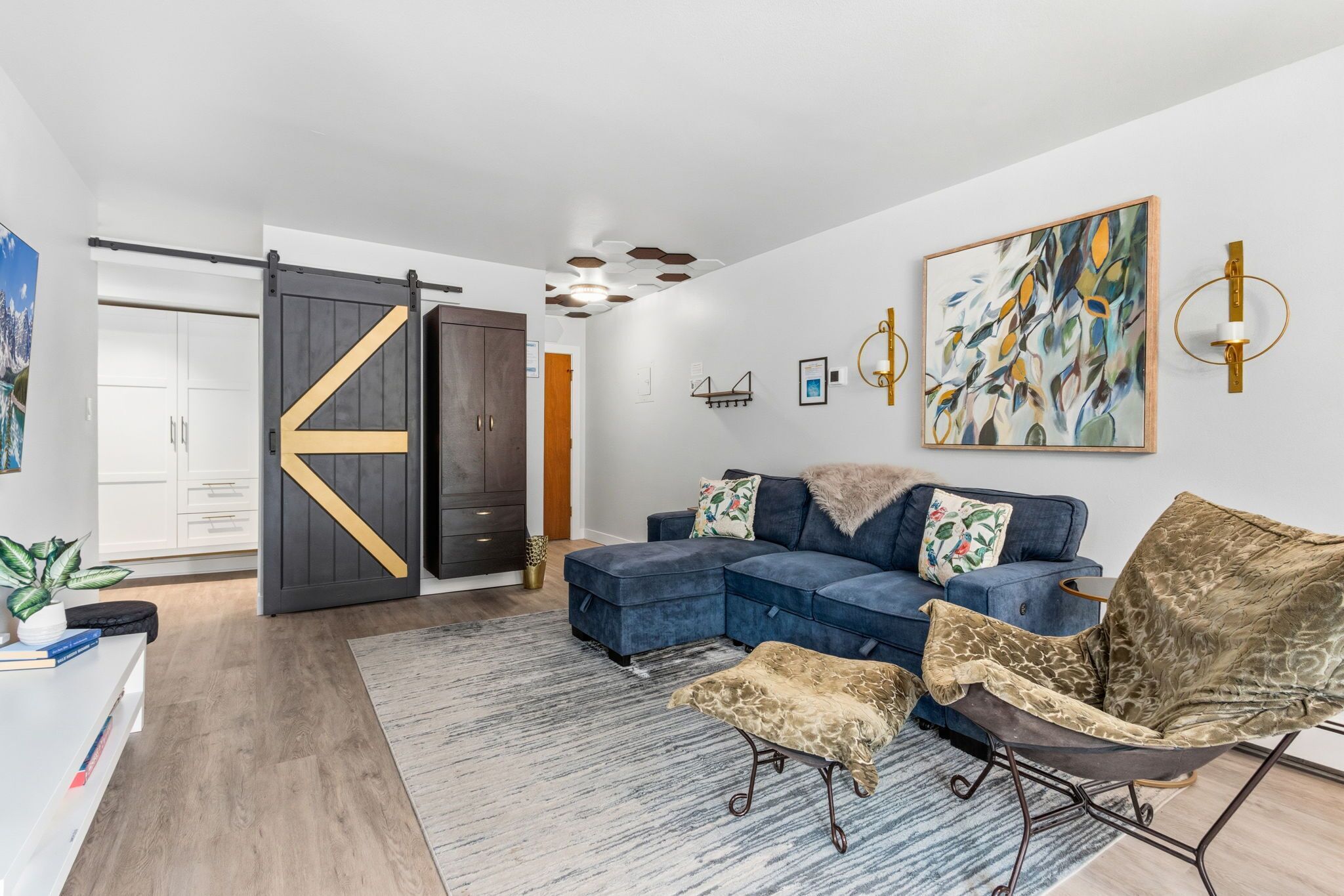 A modern living room with a sectional sofa, a unique chair, a large abstract painting, and a sliding barn door.