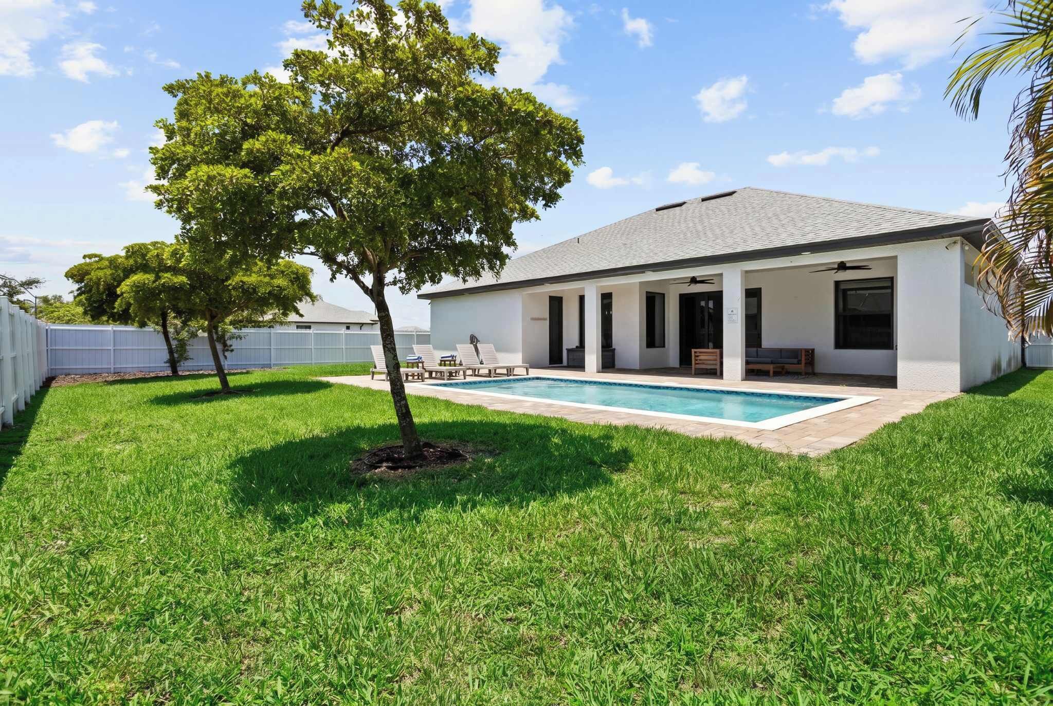 A modern house with a swimming pool, a covered patio, and a well-maintained lawn.