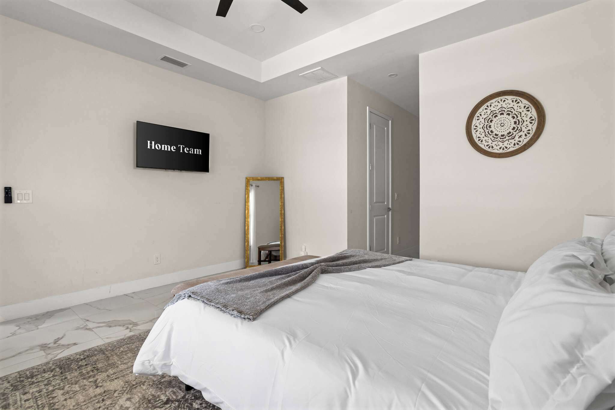 A bedroom with a bed, a flat-screen TV, a mirror, and a decorative wall piece.