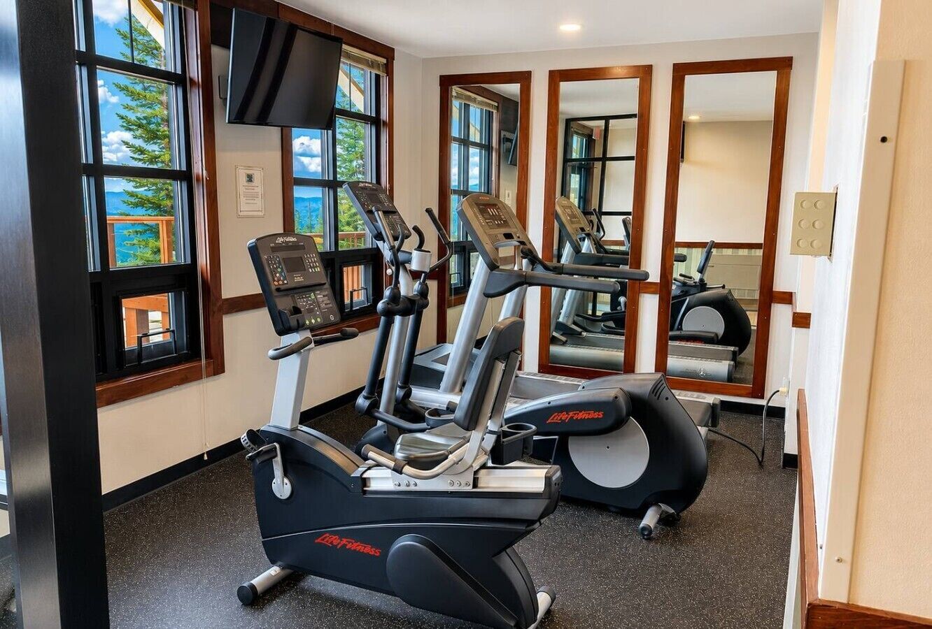 Ein Fitnessstudio mit Cardiogeräten, Spiegeln und großen Fenstern mit Blick auf eine schöne Aussicht.