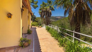 Un camino que lleva a un edificio con cerca blanca, plantas en macetas y vistas a un paisaje montañoso.
