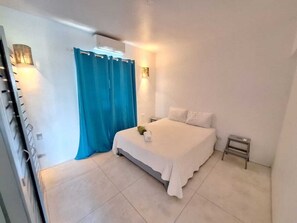 A bedroom with a bed, a nightstand, a small table, a curtain, and a wall-mounted light fixture. - Rare Sea View Gem Steps from the Village for 4per (Las Terrenas)