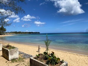 A beach with clear water, a sandy shore, and a distant island with trees. - Rare Sea View Gem Steps from the Village for 4per (Las Terrenas)