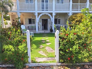 A two-story building with a white balcony, a front door, and a garden with stepping stones. - Rare Sea View Gem Steps from the Village for 4per (Las Terrenas)