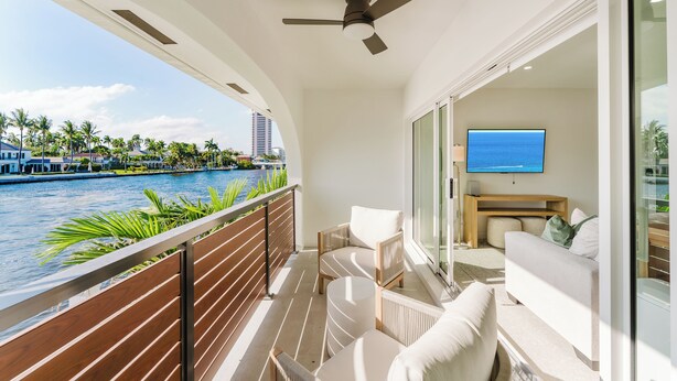 A balcony with a view of the water, a ceiling fan, a TV, and a sofa. - Villa Sirena: Boca Waterfront Escape (Boca Raton)