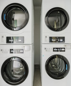 A row of four commercial laundry machines with control panels, arranged in a narrow space.