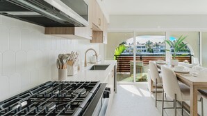 A modern kitchen with a gas stove, white cabinets, and a dining area with a table and chairs. - Villa Sirena: Boca Waterfront Escape (Boca Raton)