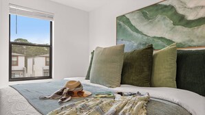 Ein Schlafzimmer mit großem Fenster, einem Bett mit vielen Kissen, einer Decke und einem Hut auf dem Bett.