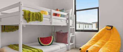A bunk bed room with a view of buildings outside, a window, and a large stuffed banana toy.