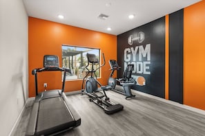 Ein Fitnessraum mit Laufbändern, Crosstrainern und einer Wand mit der Aufschrift 'GYM'.