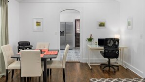 Une pièce moderne comprenant une table à manger, des chaises, un bureau avec un fauteuil, un réfrigérateur et une plante.
