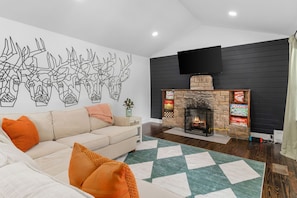 Ein Wohnzimmer mit einem beigefarbenen Sofa, einem gemusterten Teppich, einem Kamin mit Steinverkleidung und einem an der Wand montierten Fernseher.