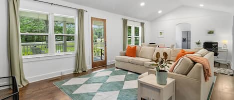 A modern living room with a sofa, a coffee table, and a view of a garden through large windows.