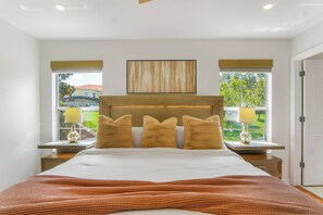 Ein modernes Schlafzimmer mit einem großen Bett, zwei Nachttischen mit Lampen, einer Kopfteil und Blick ins Freie.