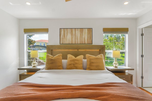 A modern bedroom with a large bed, two bedside tables with lamps, a headboard, and a view of the outside. - Encantada 4BR Private Pool Near Disney (Kissimmee)