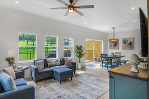 Ein geräumiges Wohnzimmer mit einer Eckcouch, einem Essbereich mit Tisch und Stühlen und großen Fenstern mit Blick ins Freie.