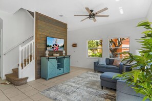 A living room with a staircase, a television, a blue cabinet, a gray sofa, and a ceiling fan. - Encantada 4BR Private Pool Near Disney (Kissimmee)