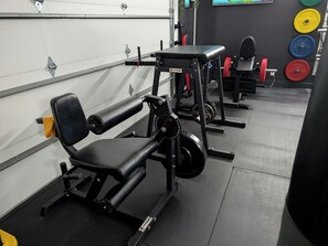 A gym with weightlifting equipment, benches, and a wall-mounted mirror.