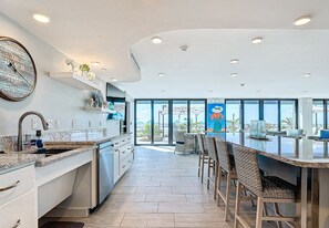 Une cuisine moderne dotée d’un grand îlot central, d’appareils électroménagers intégrés et offrant une vue sur l’extérieur.