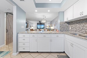 A modern kitchen with white cabinetry, a granite countertop, and a backsplash with black and gray tiles. - ⛱️Beachfront | Heated Swimming Pool | Caper Beach Club 313⛱️ (Fort Myers Beach)
