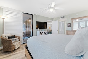 Ein Schlafzimmer mit einem großen Bett, einem Korbstuhl, einem Fernseher und einem Deckenventilator.