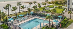 Un espace piscine doté de chaises longues et de parasols, entouré de palmiers et offrant une vue sur la plage.