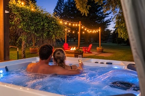 Un couple dans un bain à remous, avec un foyer et des guirlandes lumineuses en arrière-plan.
