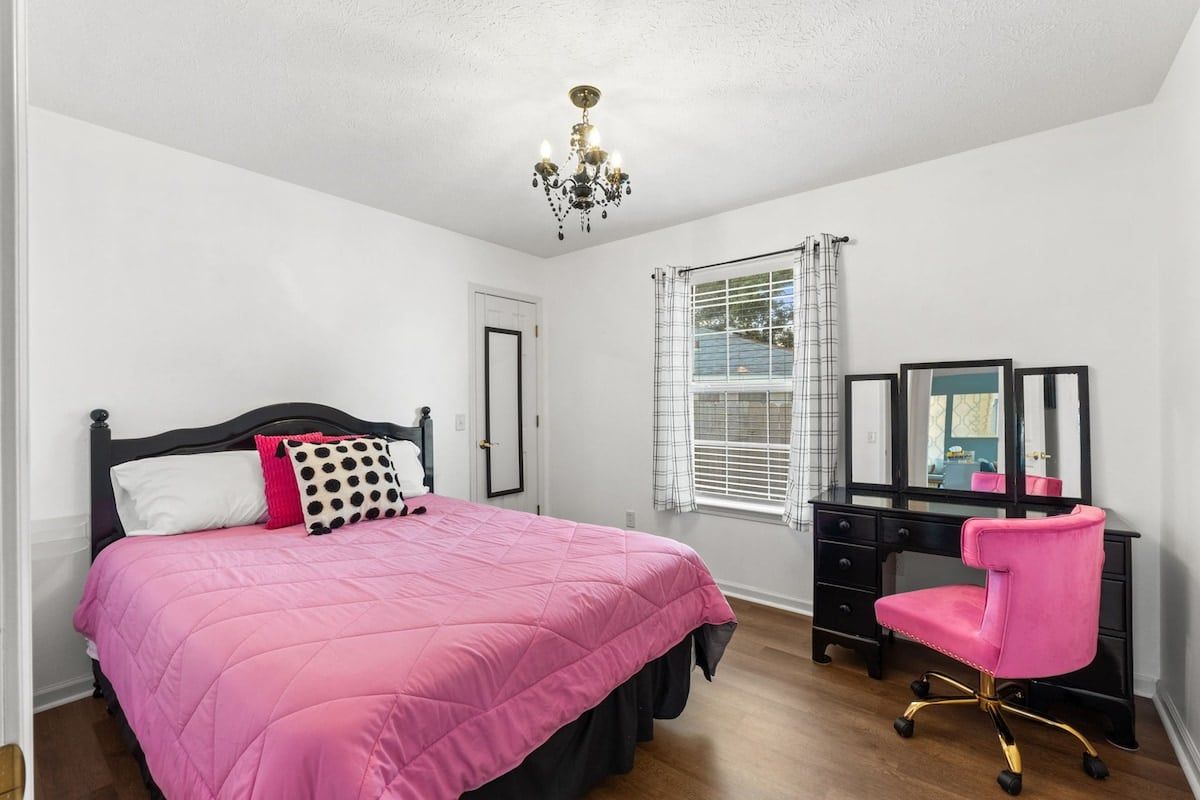 Une chambre à coucher avec un lit, un bureau, une chaise, un miroir et une fenêtre avec des rideaux.