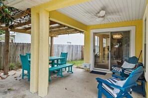 Ein überdachter Patio-Bereich mit Tisch und Stühlen, einer Schiebetür und einem Deckenventilator.
