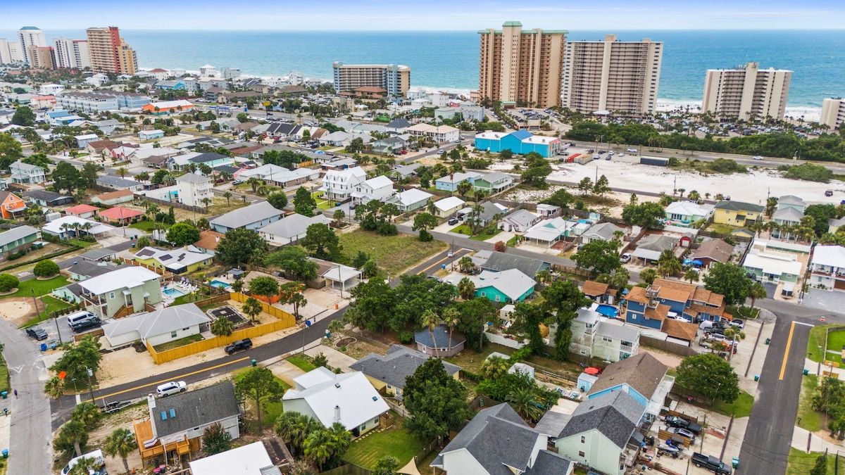 Vista aérea de una zona residencial con casas, carreteras y una playa al fondo.