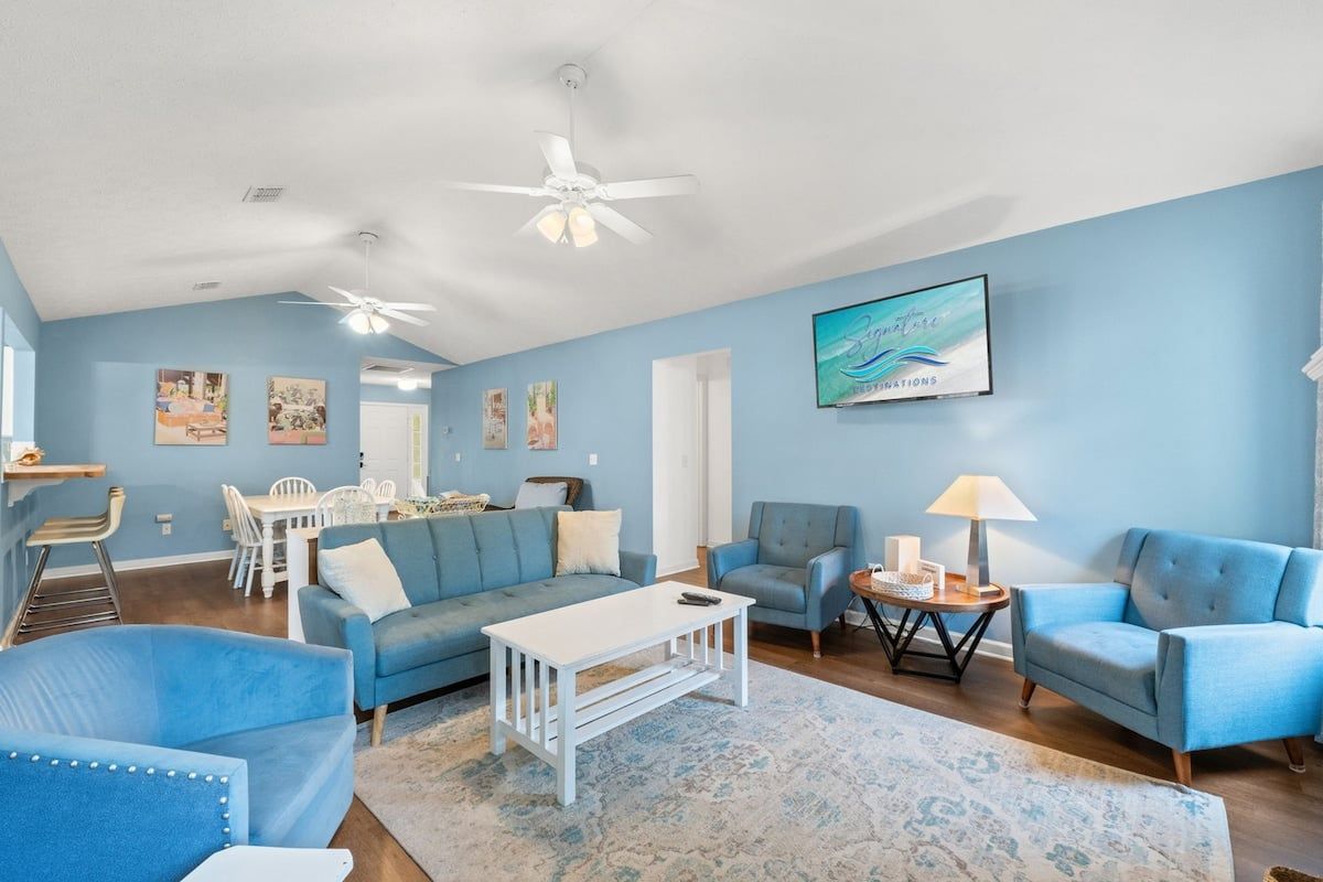 Un salon spacieux avec un canapé bleu, une table basse blanche et un ventilateur de plafond.