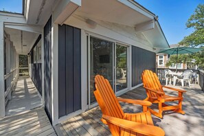 Eine überdachte Terrasse mit Schiebetüren, zwei orangefarbene Adirondack-Stühle und ein Tisch mit Sitzgelegenheiten.