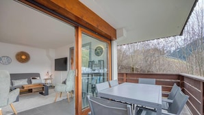 Un soggiorno moderno con una porta vetrata che dà su un balcone, un'area pranzo con tavolo e sedie, e un angolo relax con divano e poltrone.
