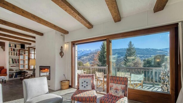 Un salon chaleureux avec une cheminée, une bibliothèque et un balcon offrant une vue panoramique sur les montagnes.