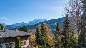 Un chalet de montagne offrant une vue sur les sommets enneigés, entouré d’arbres à feuilles persistantes.